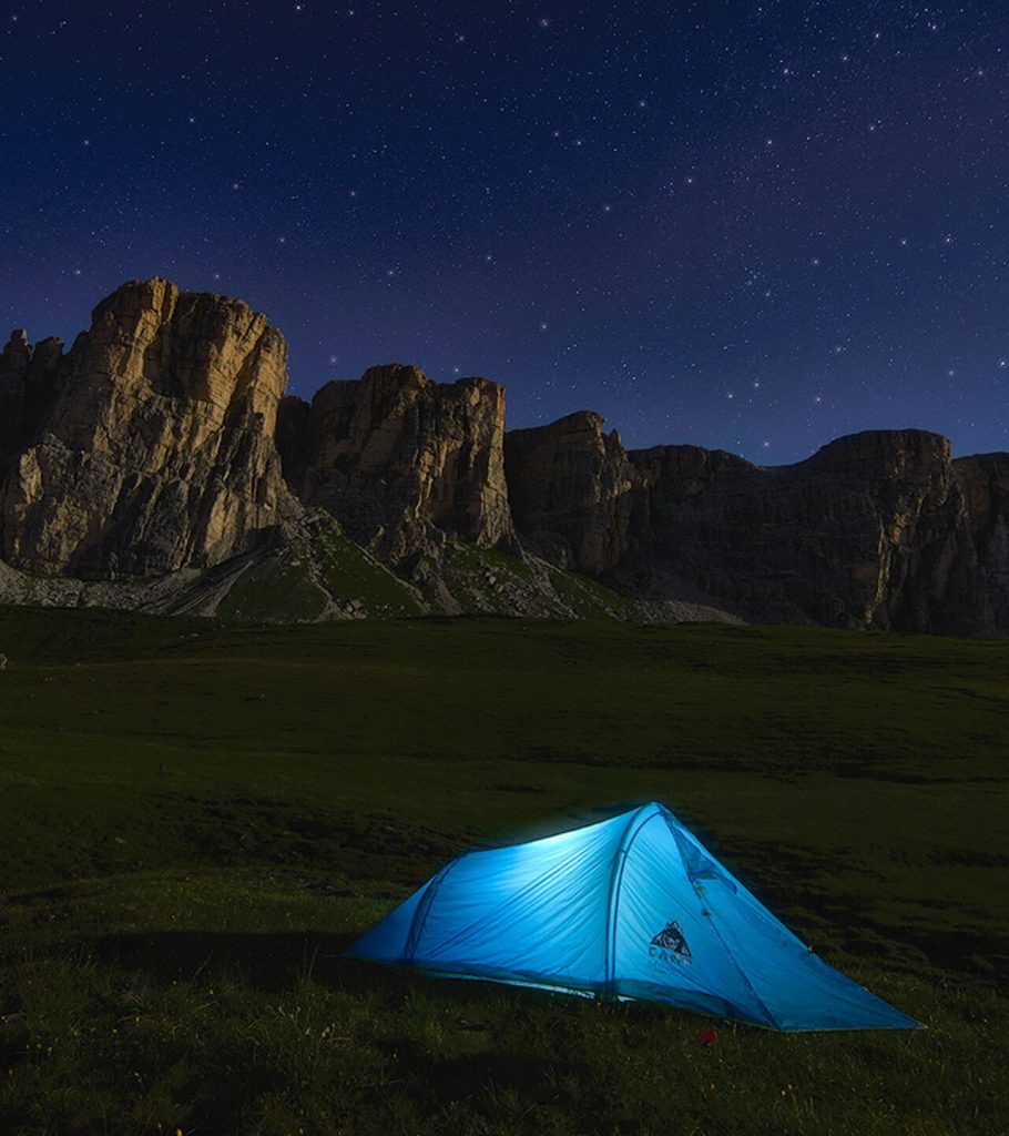 turquoise tent lit from within near mountain
